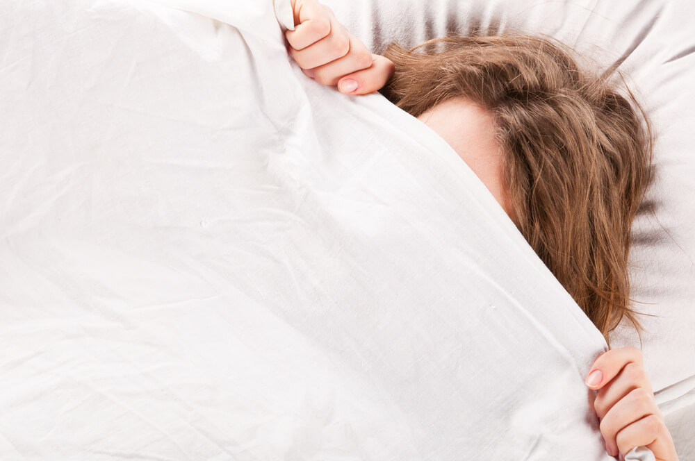 Woman hiding head under blanket